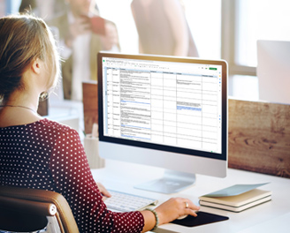 A woman in front of a computer screen displaying Excel tables