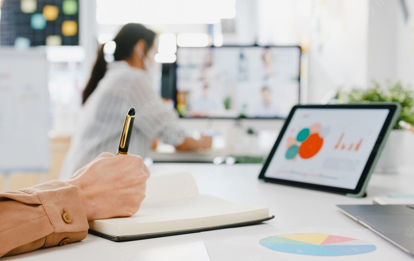 Une main prend des notes sur un cahier avec une tablette posée sur le bureau